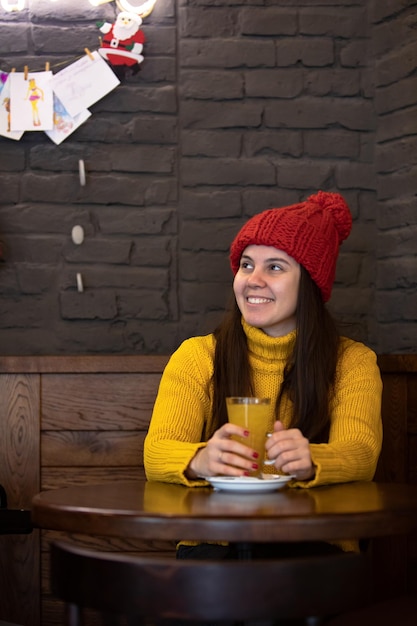 Young happy woman in red hat winter outfit sitting in cafe drinking warm up tea