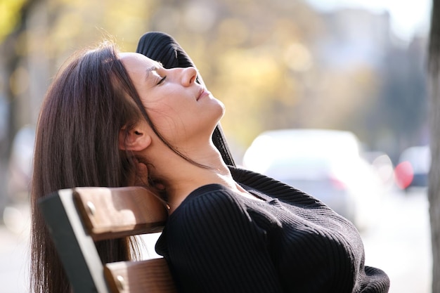 Young happy woman relaxing on city street bench on warm fall\
day wellbeing and resting from everyday rush concept