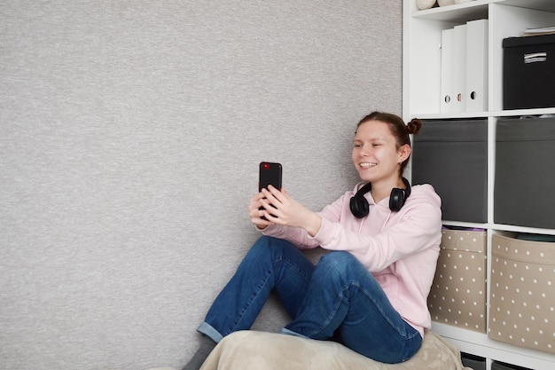 Young happy woman sitting on the couch takes a selfie and communicates with friends copy space