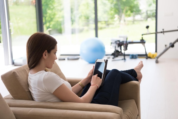 고급 주택에서 태블릿 컴퓨터와 함께 소파에 앉아 있는 젊은 행복한 여성