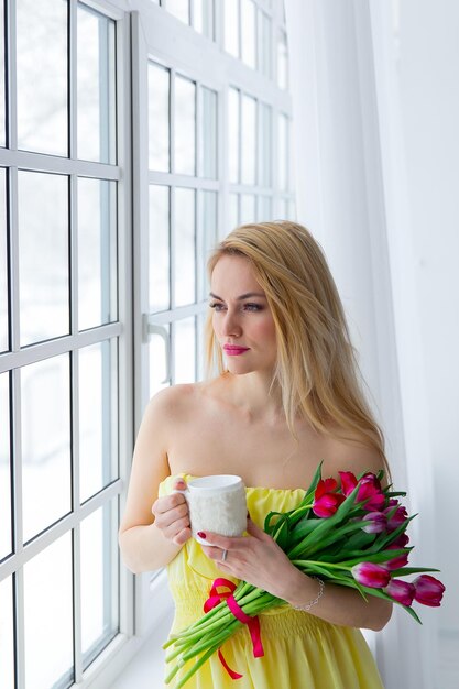 Young happy woman smiling with tulip bunch and cup tea march