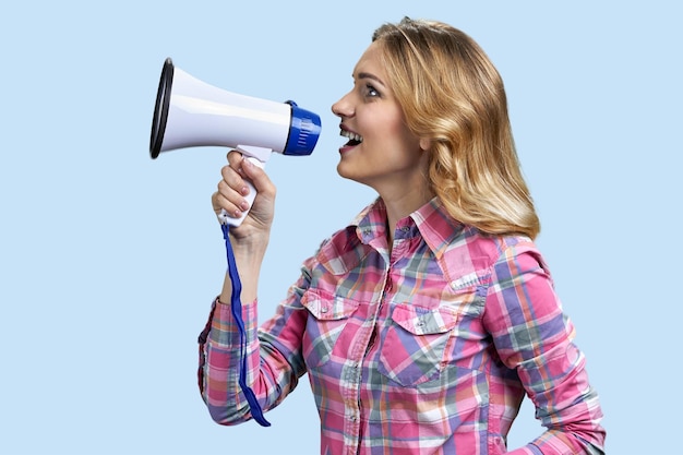 Young happy woman speaking with megaphone on light blue background side view of pretty girl talks in