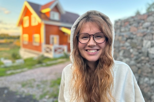 Молодая счастливая женщина стоит возле своего дома и улыбается на закате