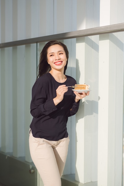 Young happy woman stands on the terrace of the hotel with dish cake in the morning. Pretty asian girl in good mood and is ready for adventures.