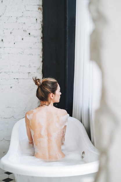 Young happy woman taking bath with foam at home treat yourself