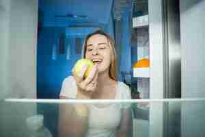 Photo young happy woman taking green apple out of refrigerator