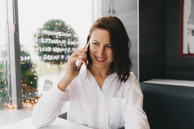 Young happy woman talking on a cell phone in a coffee shop, a lady with a beautiful smile talking on a cell phone while sitting in a cafe during lunch