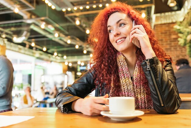 コーヒーショップで電話で話している若い幸せな女性。