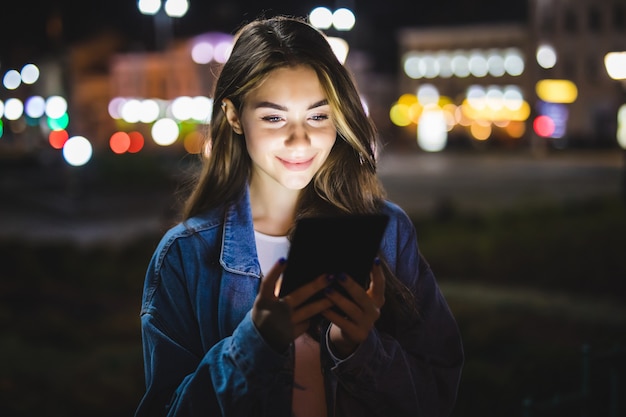 young happy woman using tablet outdoors over blurry night city lights