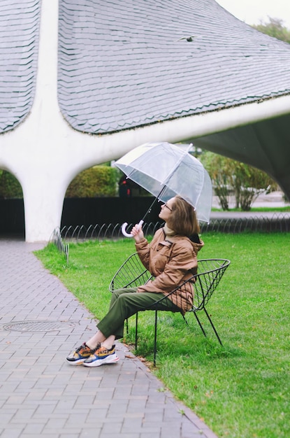 Young happy woman walking in the rain in green park with umbrella, smiling, fun. person. Fall time