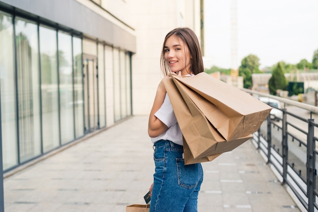 通りで屋外の買い物袋を持って歩く若い幸せな女性