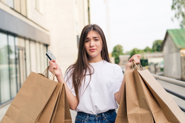 通りで屋外の買い物袋を持って歩く若い幸せな女性