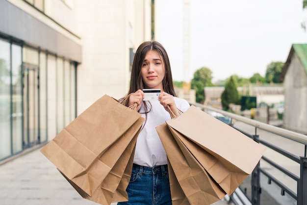 通りで屋外の買い物袋を持って歩く若い幸せな女性