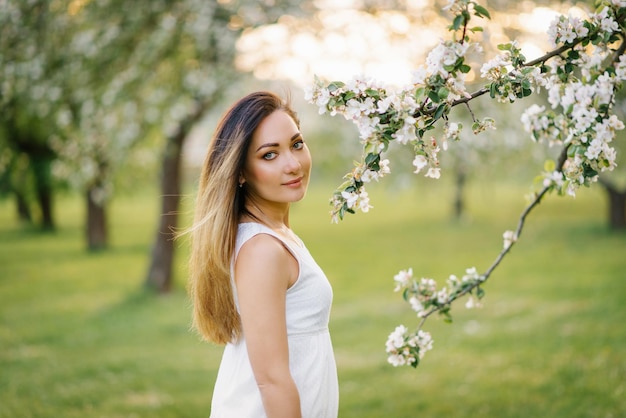 A young happy woman walks through an apple orchard among spring white flowers