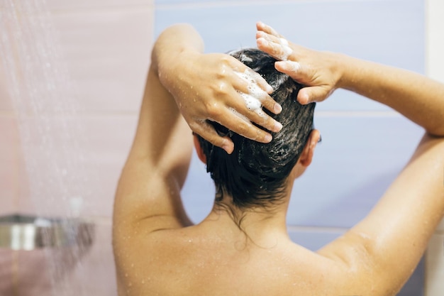 Young happy woman washing her hair with shampoo hands with foam
closeup back of beautiful brunette girl taking shower and enjoying
relax time body and hair hygiene lifestyle concept