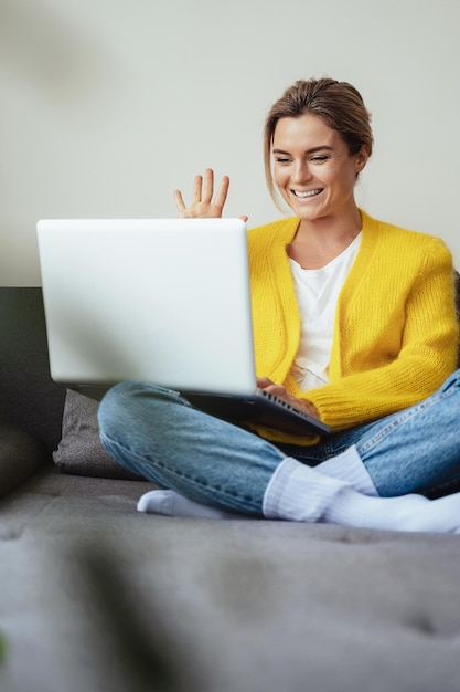 Young happy woman waving into laptop camera during online conversation by video call