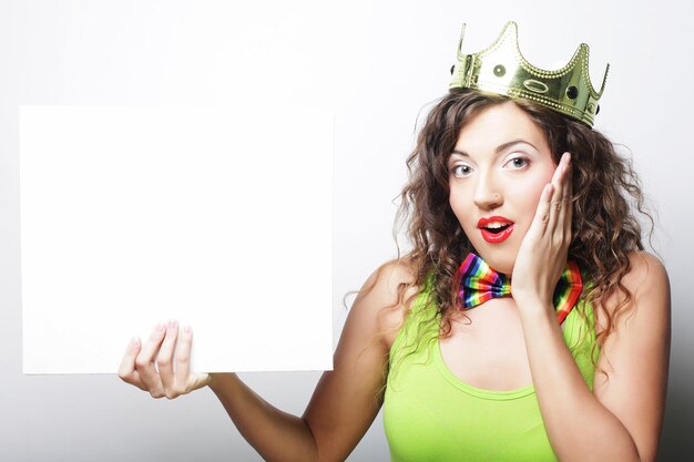 Young happy woman wearing crown holding blank sign over white background