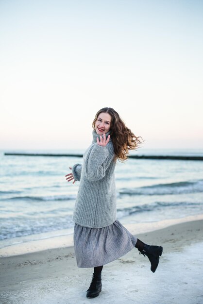 Young happy woman wearing a wool sweater running on the beach in winter during the snowfall