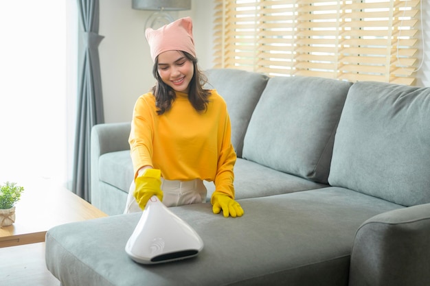 Young happy woman wearing yellow gloves and vacuum Cleaning a sofa in living room