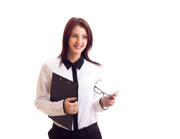 Young happy woman in white shirt and black trousers with long dark hair holding her black glasses and a folder on white background in studio