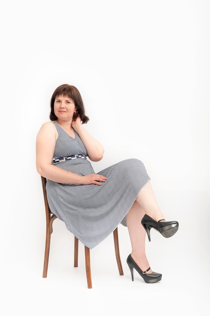 Photo young happy woman who is overweight in dress sits on chair on white background. xxl model.