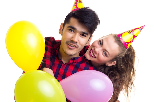 Young happy woman with chestnut ponytail and handsome man with celebrating hats blowing balloons