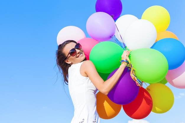 青空の背景に色の気球を持つ若い幸せな女