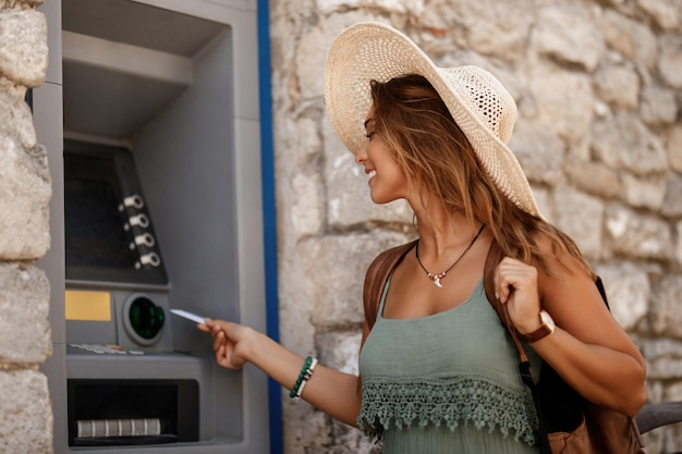 Young happy woman with credit card withdrawing money from ATM machine