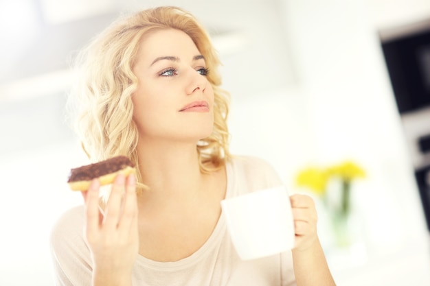 キッチンでドーナツとコーヒーと若い幸せな女性