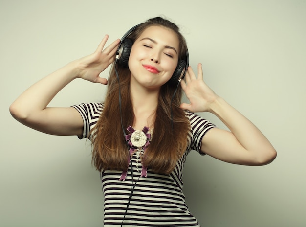 Giovane donna felice con le cuffie che ascolta musica su sfondo grigio