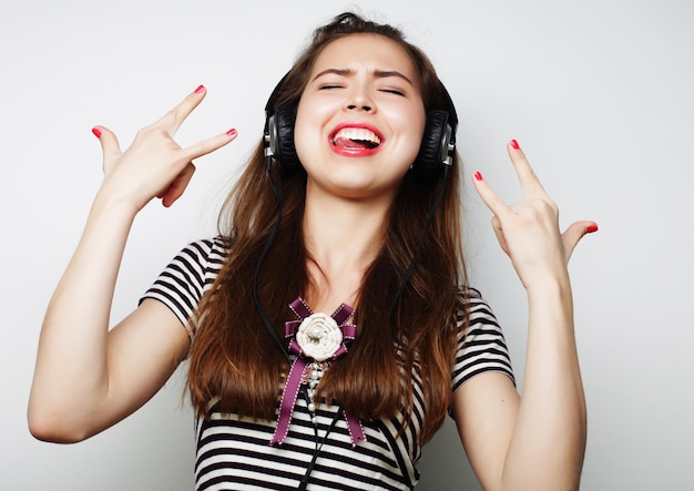 Молодая счастливая женщина в наушниках слушает музыку на сером фоне