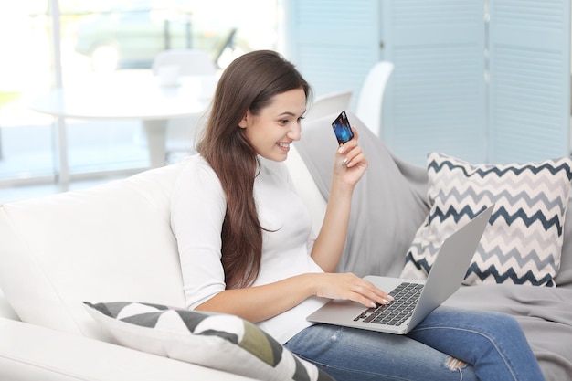 Молодая счастливая женщина с ноутбуком и кредитной картой делает покупки в Интернете