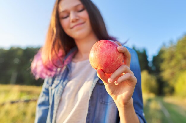 Young happy woman with red apple, girl biting an apple, sunset natural landscape background, healthy natural food