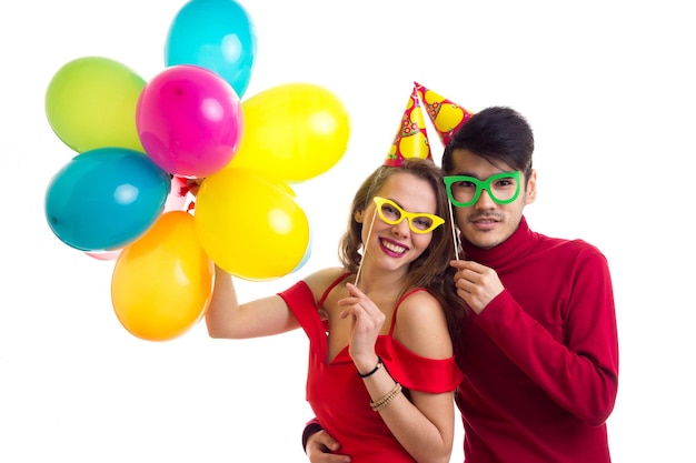 Young happy woman and young pleasant man in red plaid shirts with celebrating hats holding balloons