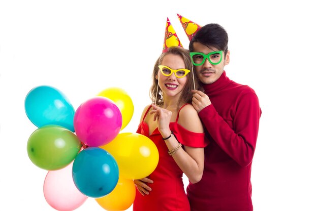 Young happy woman and young pleasant man in red plaid shirts with celebrating hats holding balloons