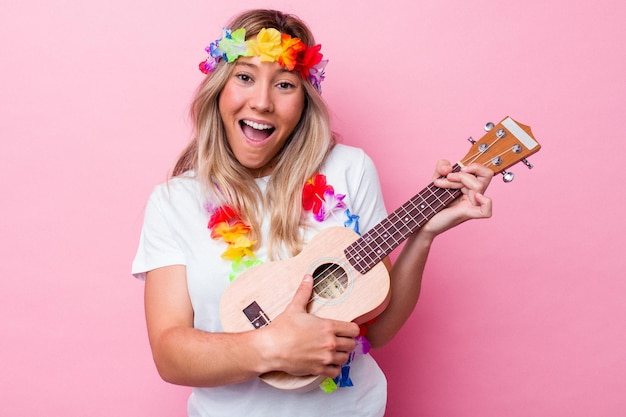 Young hawaiian woman playing a ukulele isolated on pink background