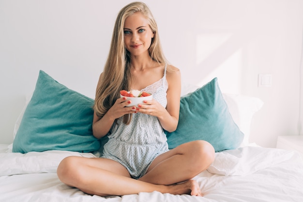 Young healthy beautiful blonde woman in the bed eating fruits
