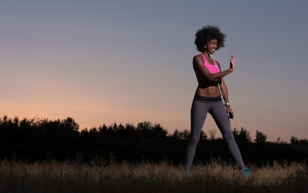 Young healthy black woman is doing stretching exercise relaxing and warm up after jogging and running in the nature beautiful summer evening