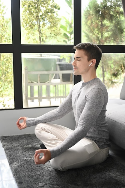 Young healthy man practicing yoga at home in lotus pose