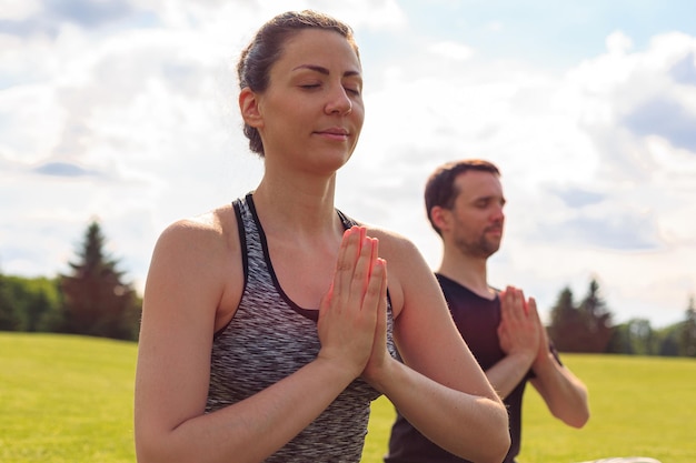 Giovane uomo e donna in buona salute che fanno yoga nel soleggiato parco estivo fitness e stile di vita sano