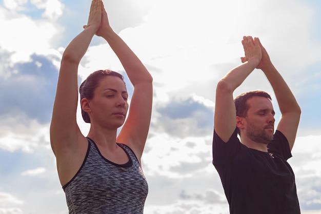 Young healthy man and woman doing yoga in the sunny summer park