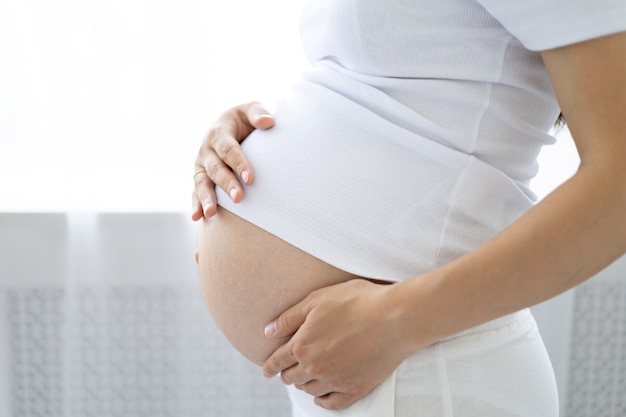 늦은 단계에 있는 젊은 건강한 임산부는 손으로 배를 껴안고 건강한 임신을 합니다
