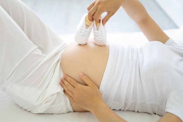 A young healthy pregnant woman at a late stage of pregnancy\
holds clothes for the baby in her hands the pregnant woman is going\
to the maternity hospital