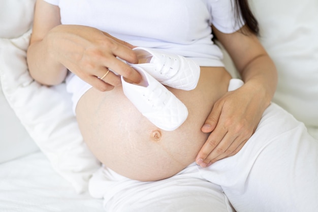 A young healthy pregnant woman at a late stage of pregnancy\
holds clothes for the baby in her hands the pregnant woman is going\
to the maternity hospital