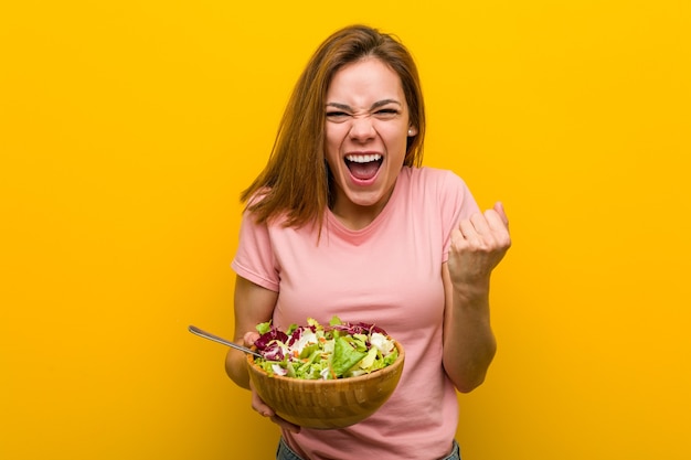 のんびりと興奮して応援するサラダを持っている若い健康な女性。利佳國際電子。