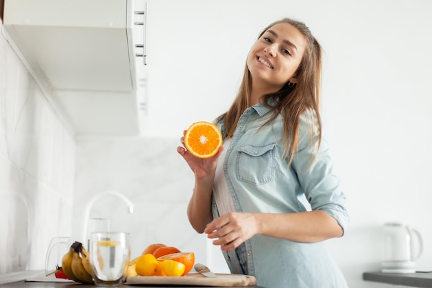 現代のキッチンでカットオレンジでポーズをとる健康な若い女性