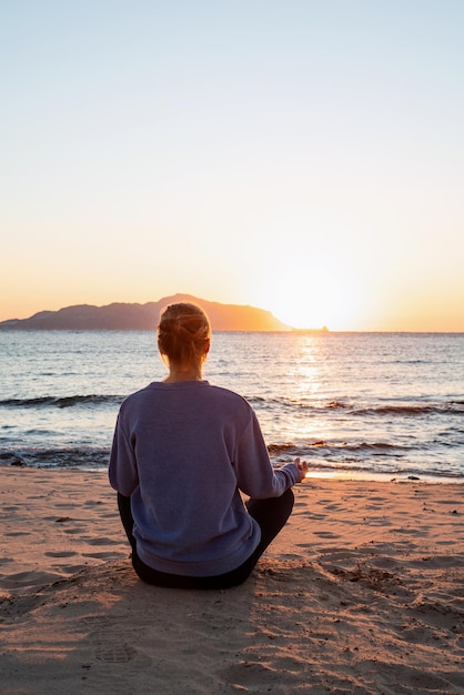 Young healthy woman practicing yoga on the beach at sunrise