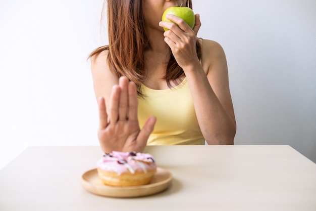 手を使用して若い健康的な女性はデザートやお菓子を押し出して青リンゴを選ぶ