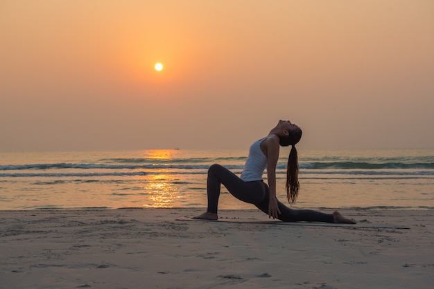 Young healthy Yoga woman practicing yoga pose on the beach at sunrise