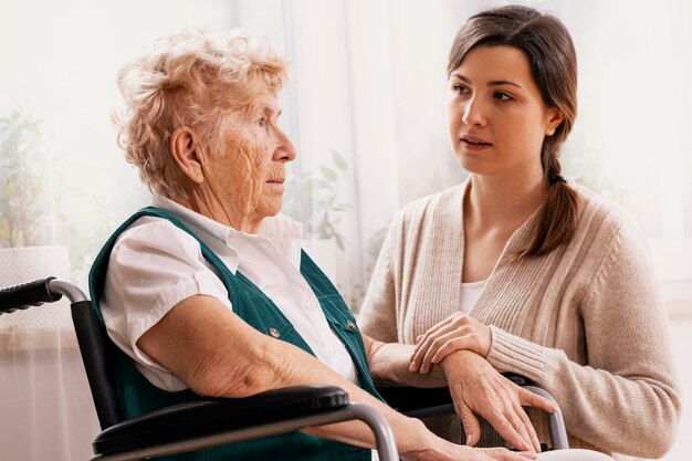 Photo young helpful granddaughter helps her grandmother get up from her wheelchair